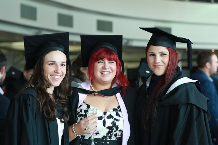 Three female graduates posing, one with a glass of wine at their graduation celebration