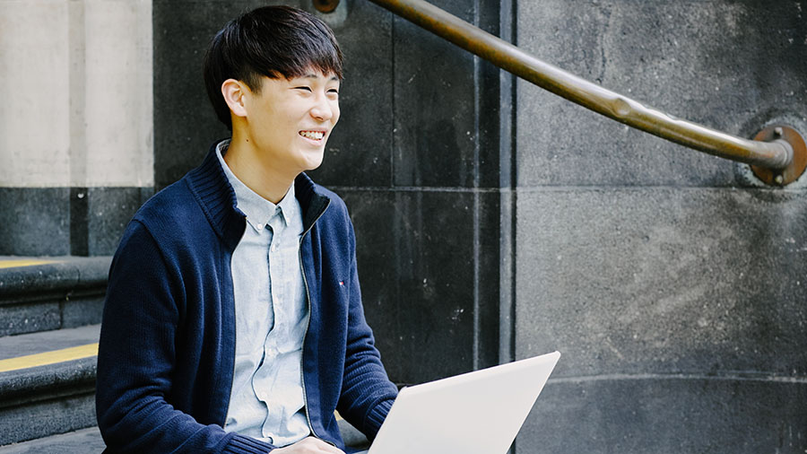 A student sits outside Queen Street with a laptop.