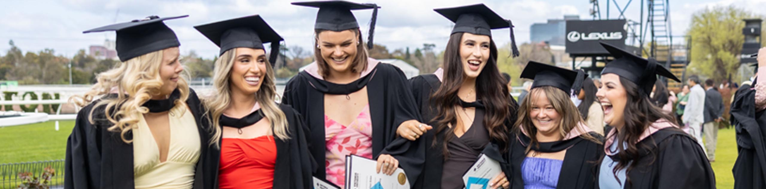 A VU student wearing the graduation gown and hat smiles into the camera, with the floating VU branded diamond.