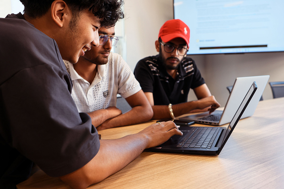 3 men collaborate around a laptop 