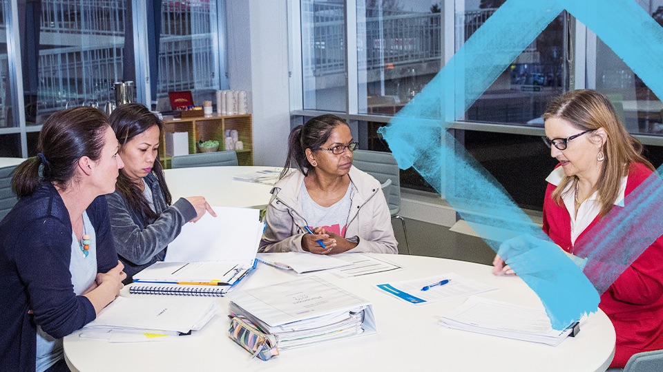 Students sitting around a table. At the other end of the table is a teacher.