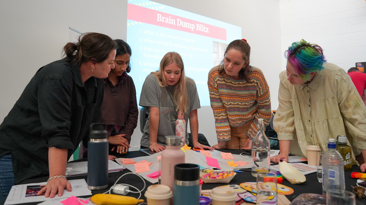 A teacher and students around a table with a large piece of paper covered in sticky notes.