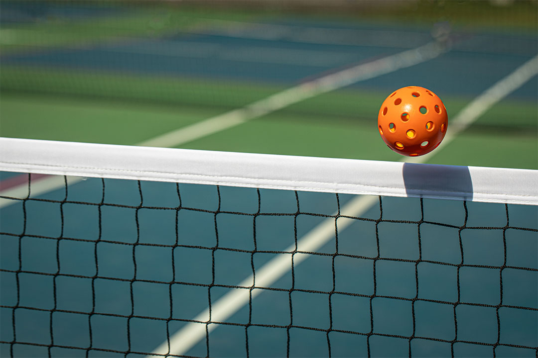 Orange pickleball sailing over net.