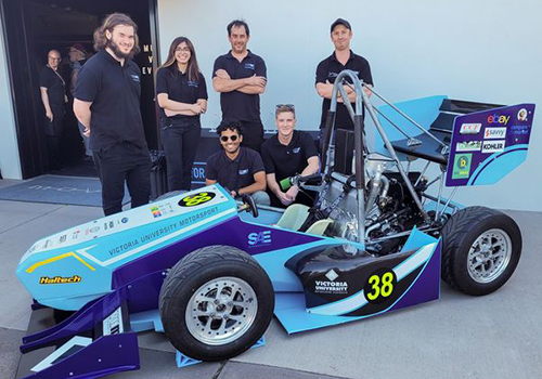 Students in Victoria U niversity T-shirts pose with a racing car in VU colours