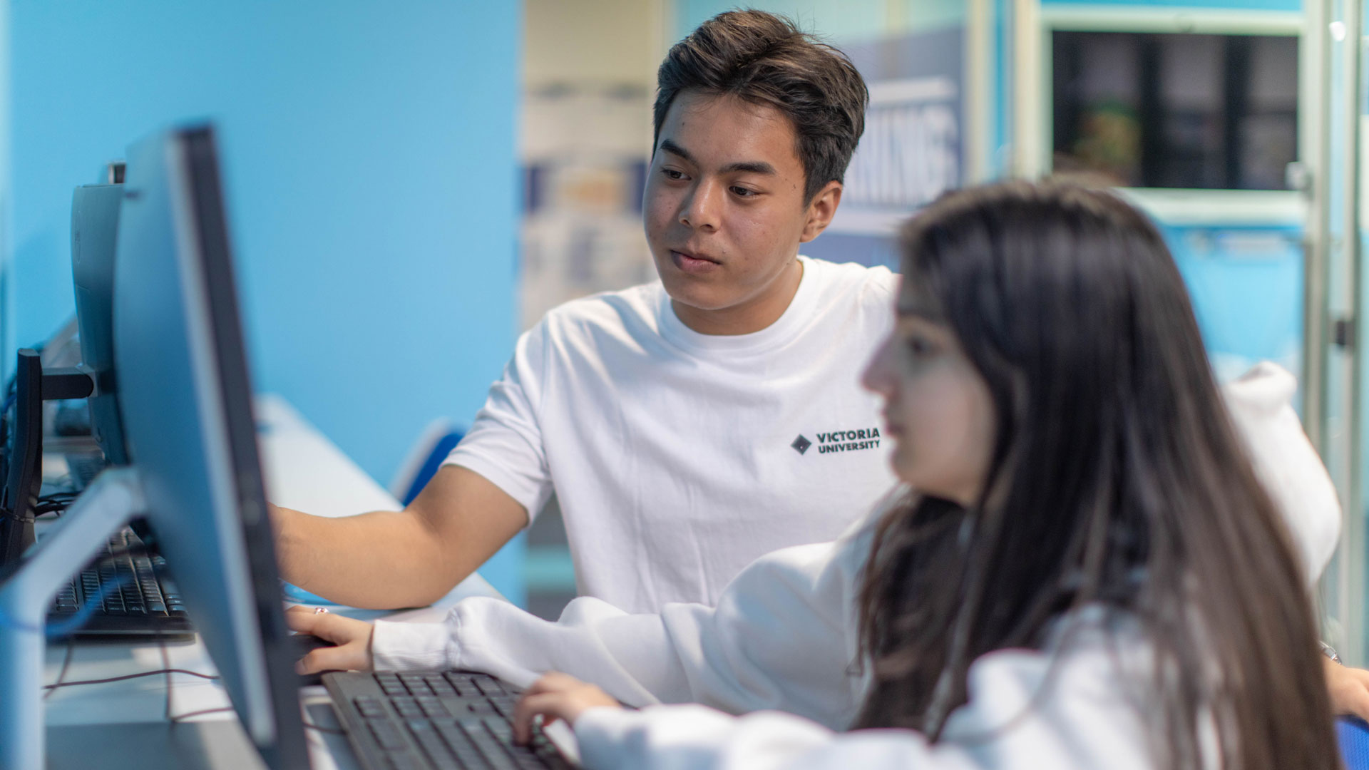 A student representative from VU Sydney sitting with a student on the computer. The representative is pointing to something on the screen.