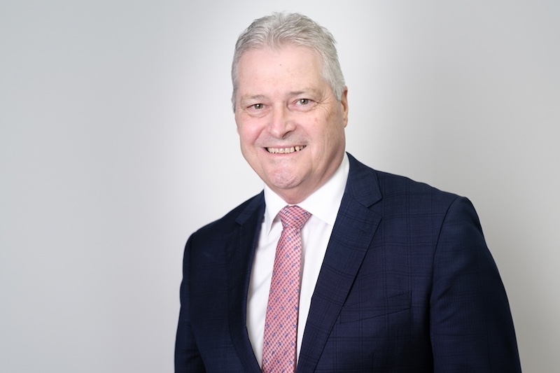 A smiling man in a blue professional suit and a pink tie