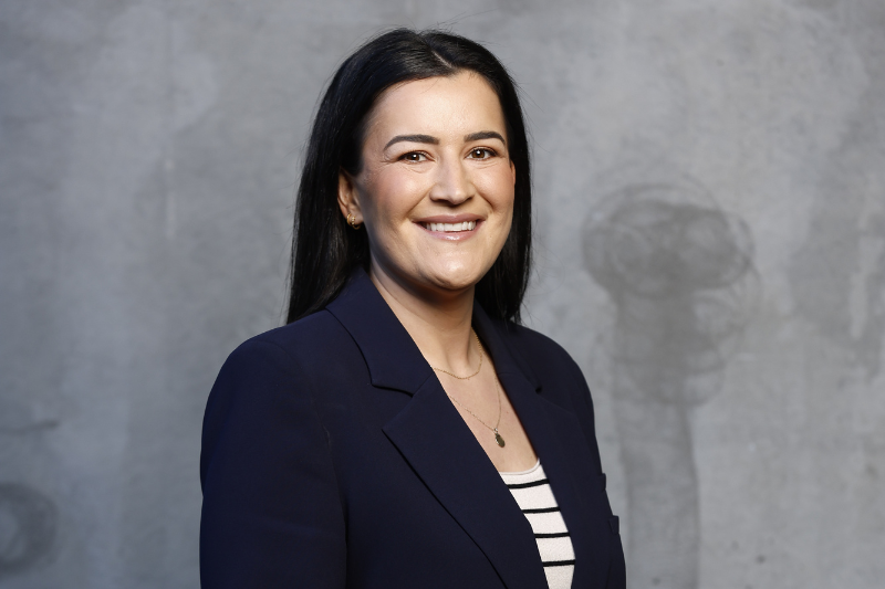 A young woman in professional suit smiles in front of a grey background