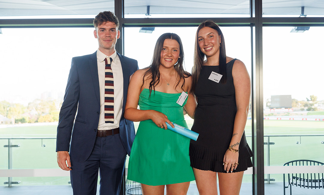 A young man in a suit poses with two women in formal summer dresses