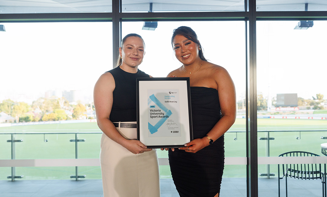 Two young, strong-looking women pose with a Victoria University award