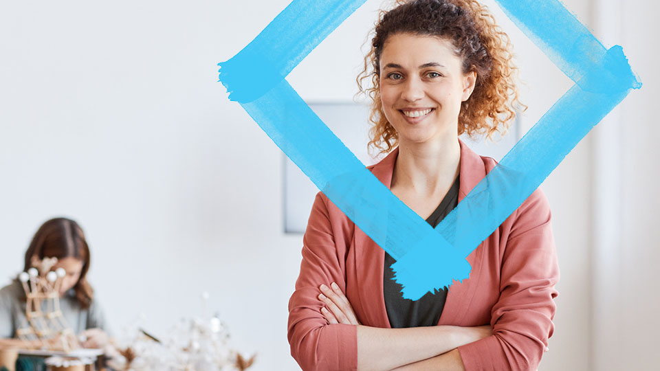Portrait of a woman with curly hair, wearing a red cardigan, smiling. A VU Blue diamond floats over her head.