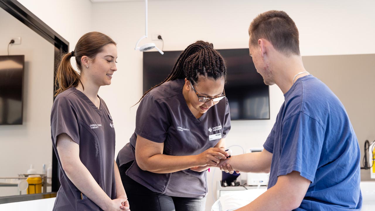 A dermal science teacher and student performing a skin check on a client.
