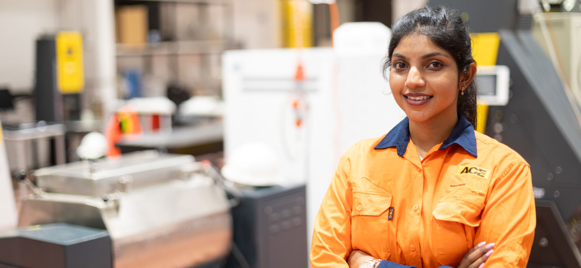 A woman in hi-vis shirt standing next to engineering equipment.