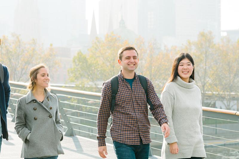 Four international students crossing bridge over Yarra River in Melbourne CBD.