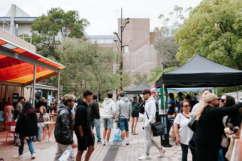 A large group of students walk among stalls on a campus courtyard