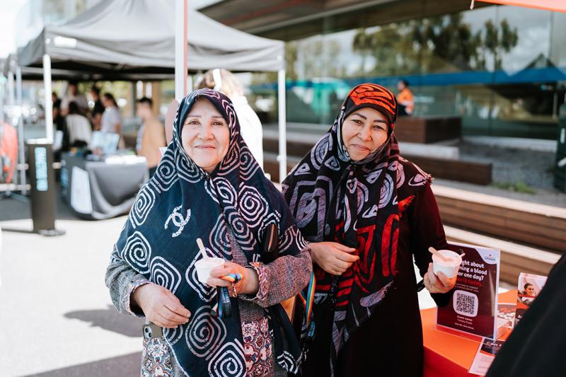 Two woman in hijabs in a sunny courtyard with stalls