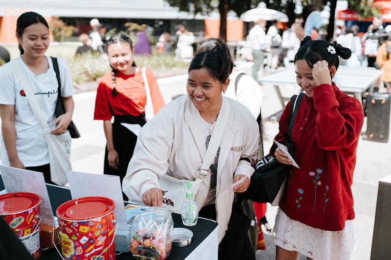 A group of young adults smile and help themselves to lollipops from a stall in a sunny courtyard