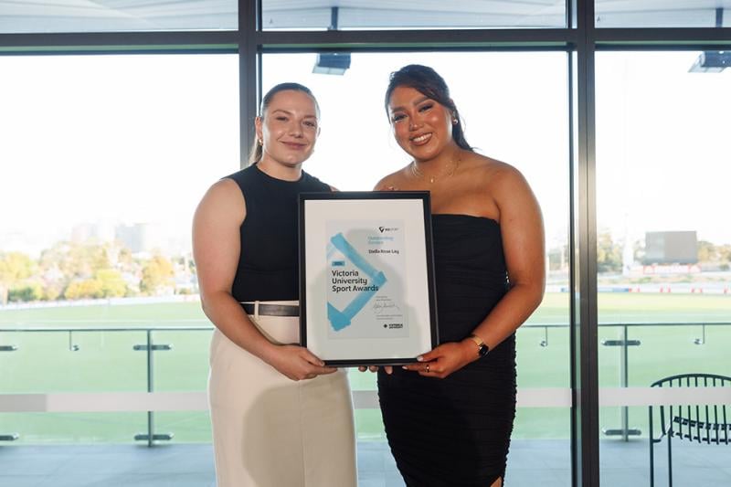 Two young, strong-looking women pose with a Victoria University award