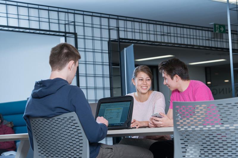 A group of students at with computers work in a modern library