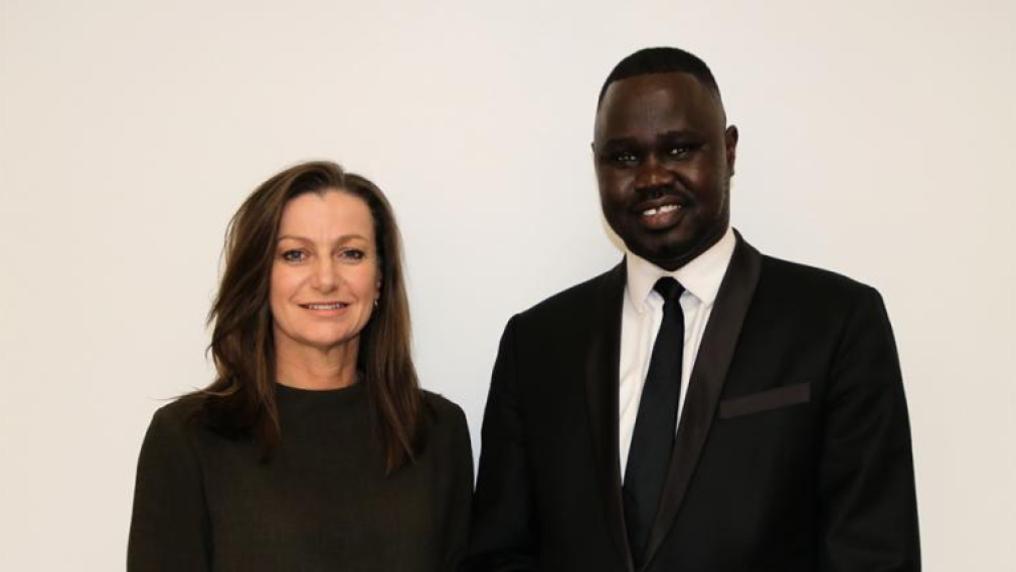 Two people standing in front of a white wall smiling at the camera.