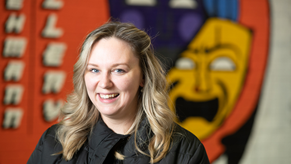 Person looking at camera and smiling. A graphic on the wall behind her is out of focus.