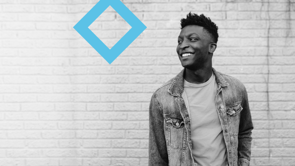 A smiling student stands next to the VU branded blue diamond.