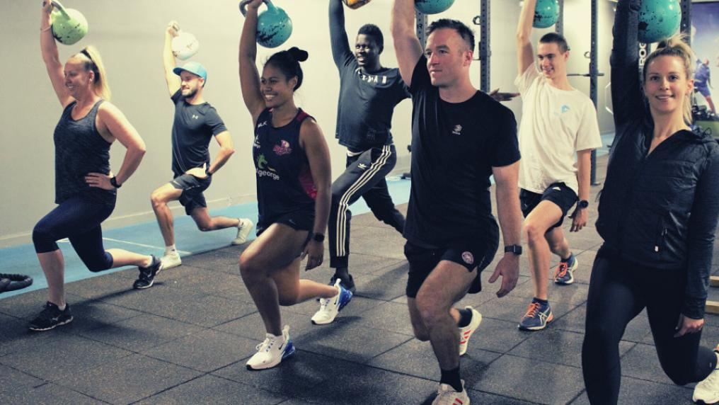 A group of people doing the same squatting exercise in a gym.