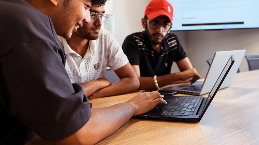 3 men collaborate around a laptop