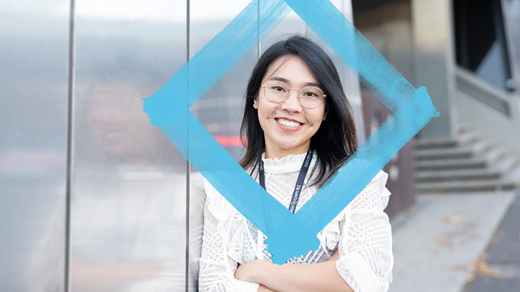Smiling student stands next to a reflective wall, with the VU blue branded diamond floating in front of them.