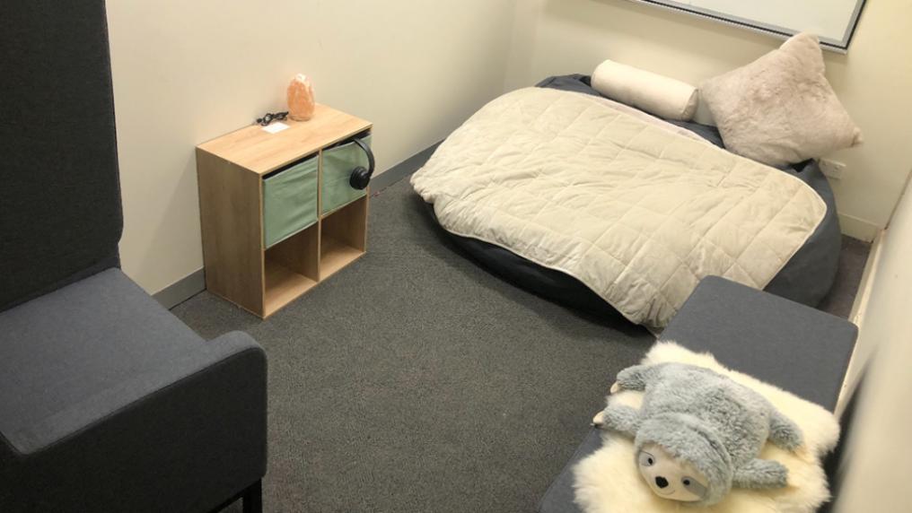 A small, comfortable room with large cushion, chair, plush toy and shelf