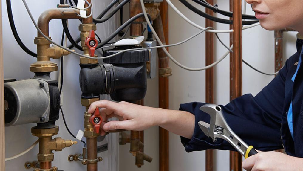 Close up of hands of a female plumber fixing pipes with a spanner.