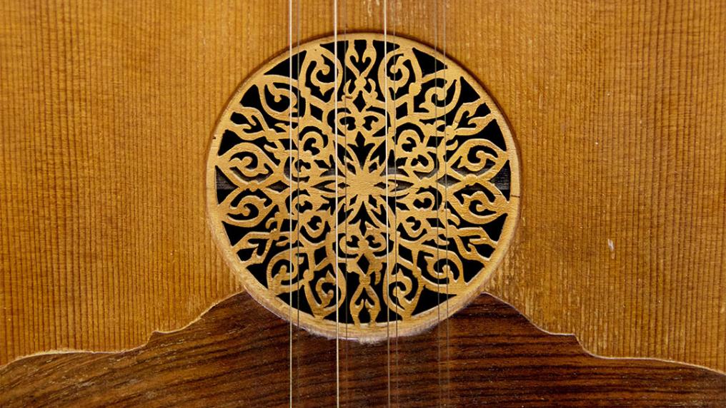 Close up at the circle of the sound hole at the soundboard of Greek traditional wooden music instrument with strings of lute decorated with flower 