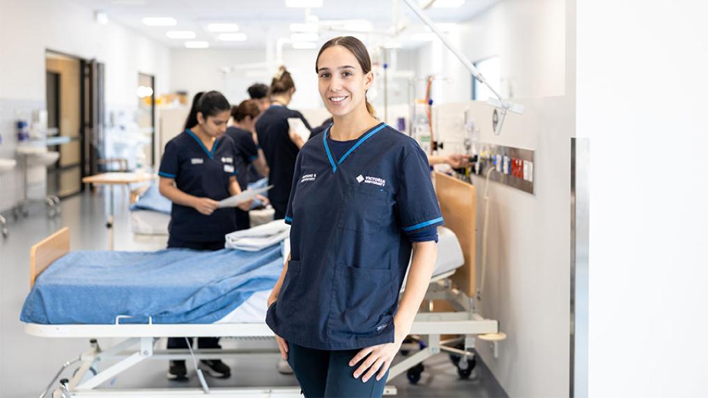 VU students getting experience working in a simulation clinic. One student stands in the foreground smiling in their VU branded uniform.
