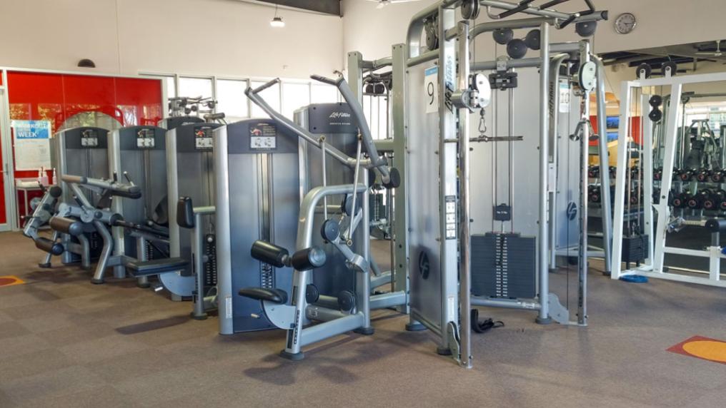 A gym floor with training machines and dumbbells.