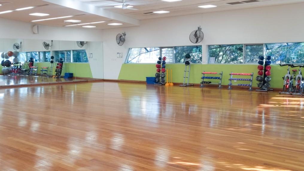 A large training room with various gym equipment on the walls. A large room-length mirror is placed on one of the walls.