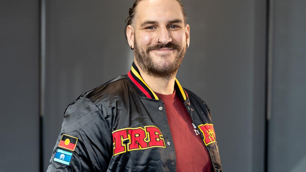 A young man poses in a jacket with the Aboriginal flag on the sleeve