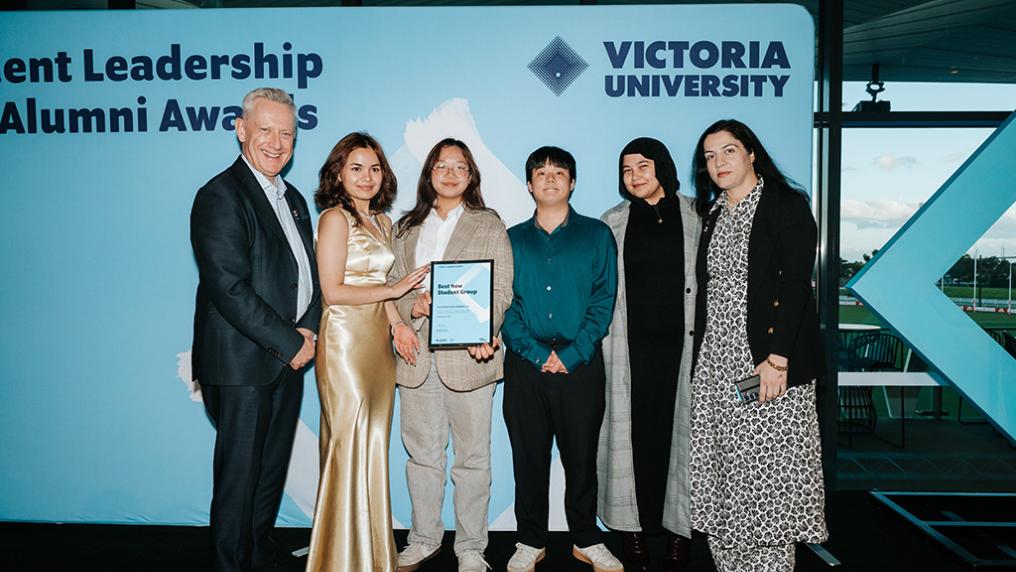 A group of young people pose with the VC against a Victoria University backdrop