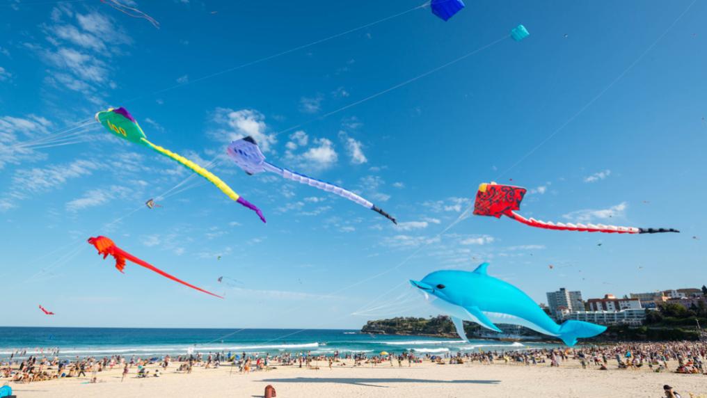 Bright kites against a blue sky against a golden sand beach