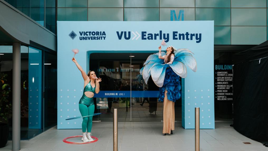 Two entertainers in costumes in front of VU Early Entry signage on campus.