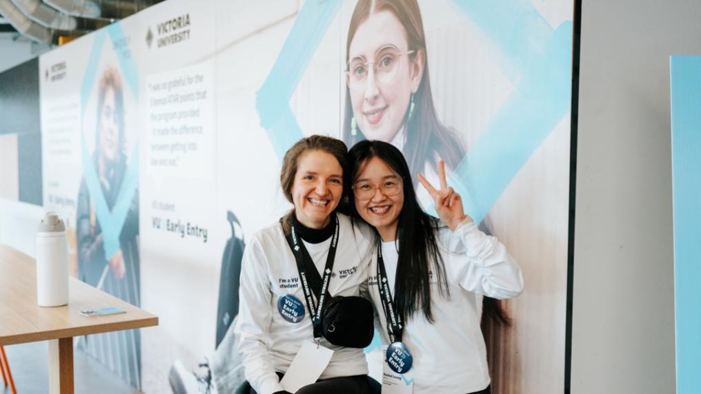 Two smiling VU advisors posing in front of large VU Early Entry boards. 