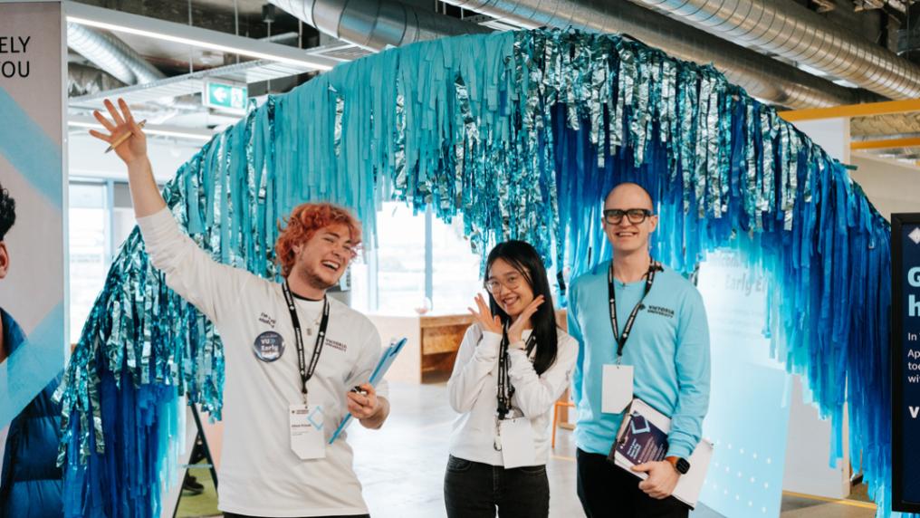 Three friendly VU advisors smiling in front of shiny decorated arch. 
