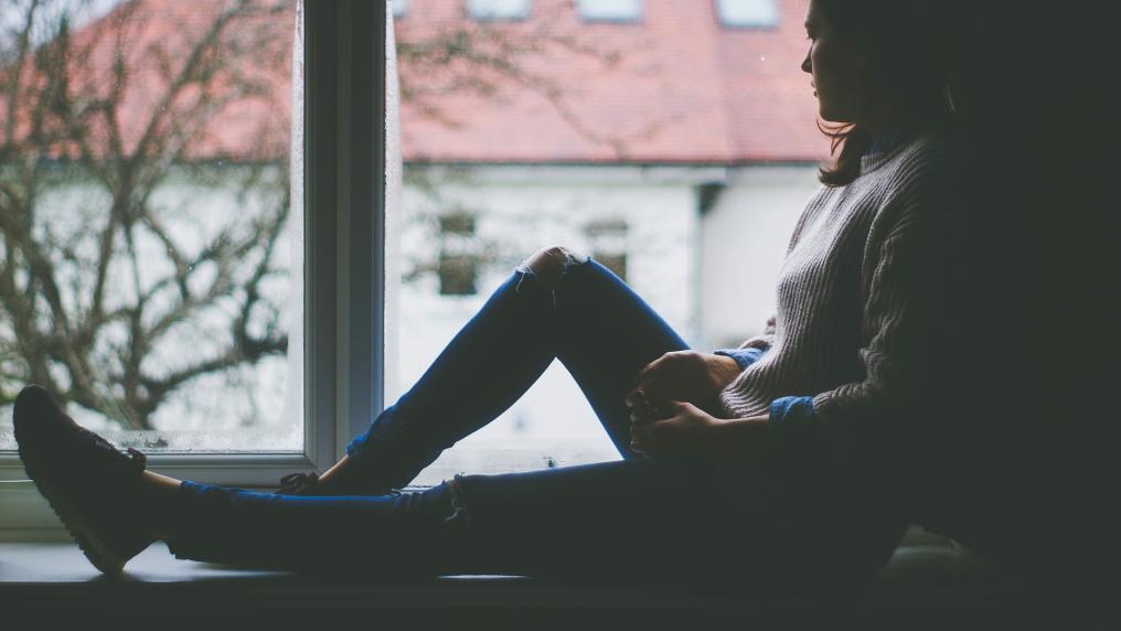 Young woman sitting on a windowsill staring out 