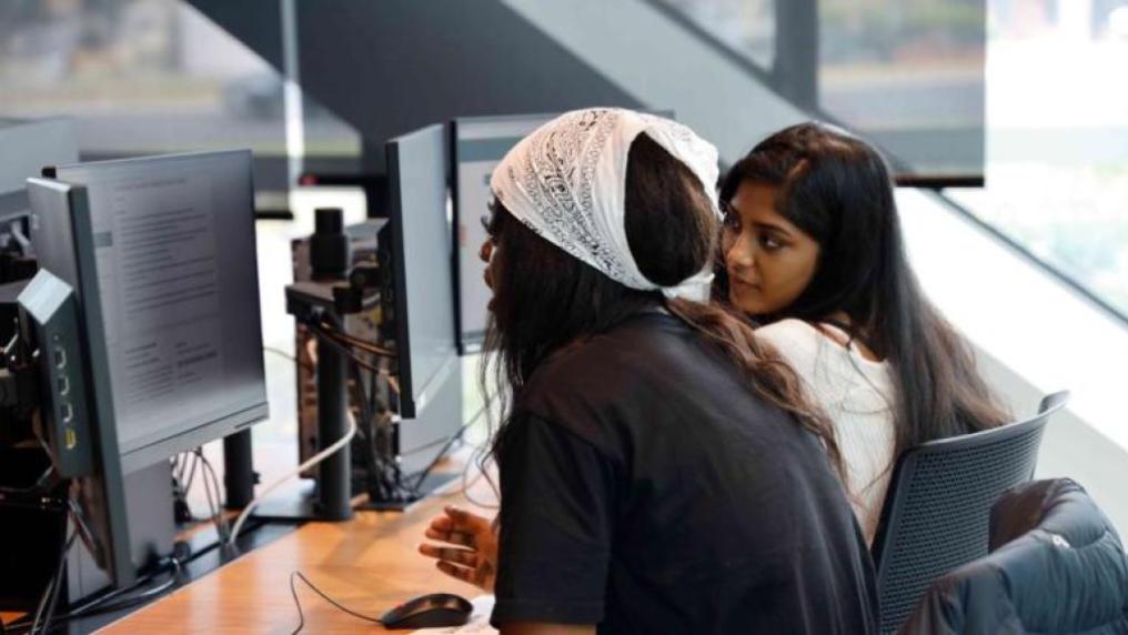 2 young women, of different cultural backgrounds, using computers in a community space