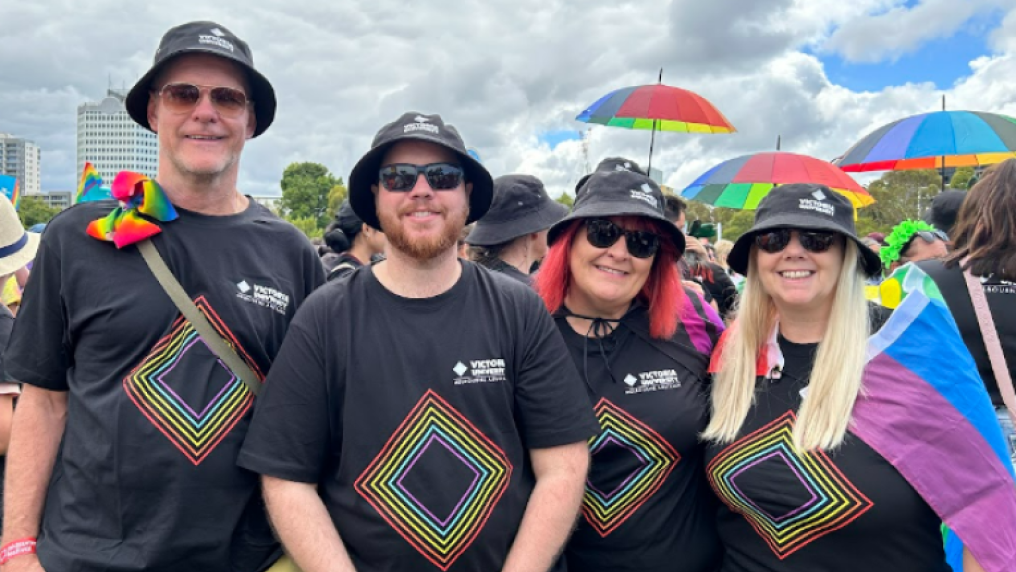 A group of smiling people in rainbow clothes with Victoria University logos